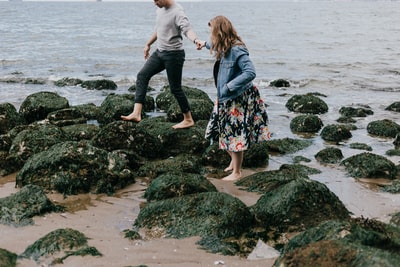 男人和女人在一起的手,踩在岩石附近的大海
